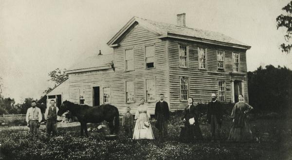 Family portrait of the Porters, standing in front of their log cabin with a horse.