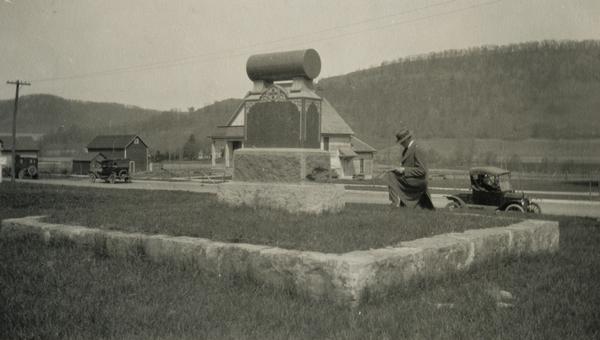 A man kneels next to a monument dedicated to the pioneers.
