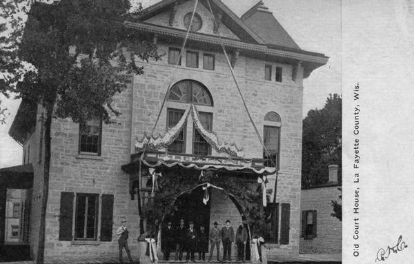 Front view of the Lafayette County courthouse, built in 1861. A group of people are standing at the entrance. Caption reads: "Old Court House, La Fayette County, Wis."