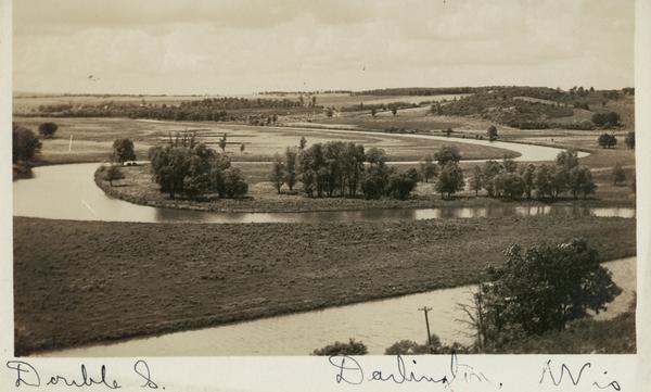 Elevated view of the Pecatonica River, which is curving from left to right, making two hairpin turns among fields and trees. Hills are in the distance.