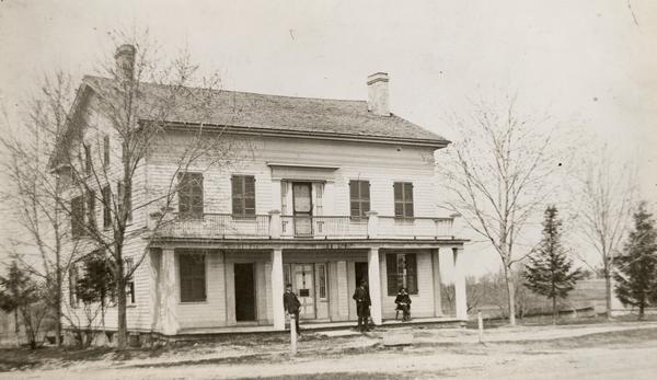 Hawks Tavern, also known as Hawks Inn, with men on the porch and trees in the yard on each side.