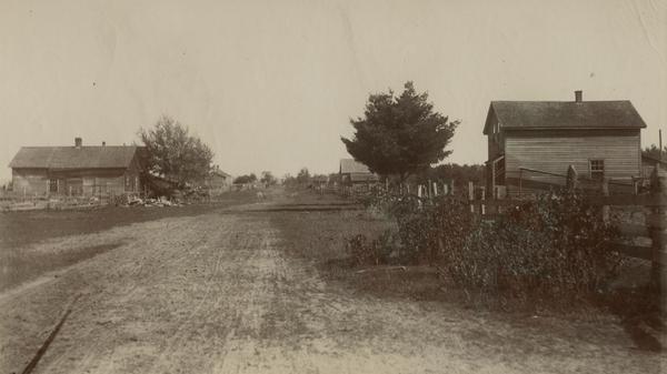 View down dirt road, with a few homes on each side of the lane.