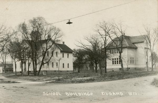 View of school buildings across an intersection, with a street light suspended from cables in the foreground. Caption reads: "School Buildings Durand Wis."