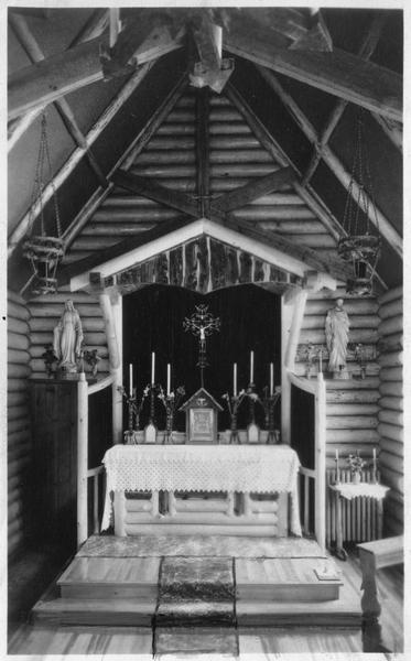 Interior view of the chapel, centering on the altar, including religious artifacts, statues, and candlesticks,.