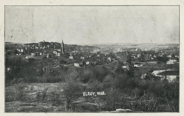 View from hill of downtown Elroy, with a church steeple and buildings.
