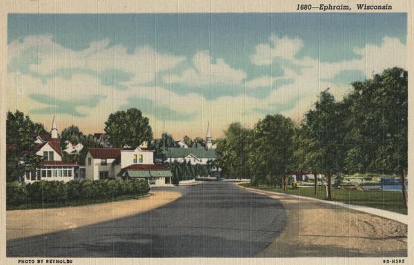View down road curving towards Ephraim. Trees are along a lawn on the right near water. Caption reads: "Ephraim, Wisconsin".