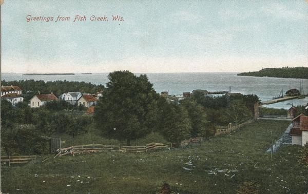 View across field and fence downhill towards the town of Fish Creek and the bay. Caption reads: "Greetings from Fish Creek, Wis."