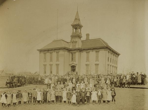 School children pose for a group portrait in front of a school.