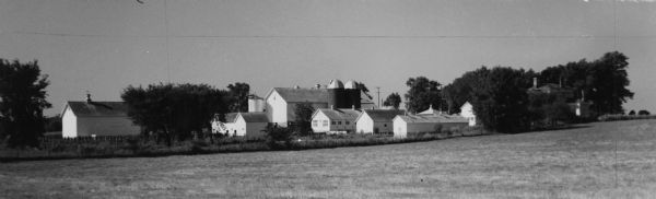 View across field toward Hoard's dairy farm with silos, barns, and trees.