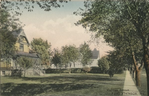 View looking down a sidewalk on the left side of Madison Avenue. Trees line the terrace, and houses and lawns are on the left. Caption reads: "Madison Avenue, Ft. Atkinson, Wis."
