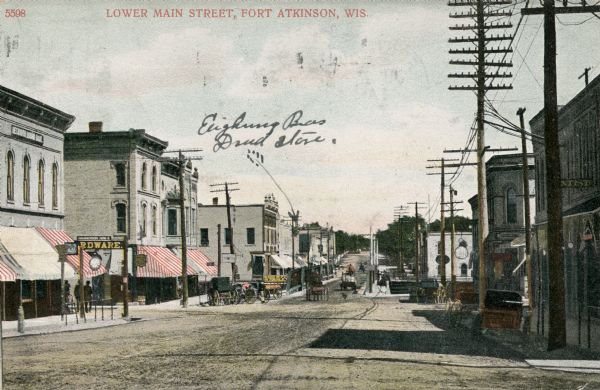 View of lower Main Street lined with electric power lines and storefronts. Caption reads: "Lower Main Street, Fort Atkinson, Wis."