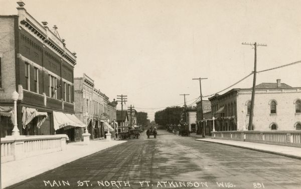 View from center of bridge looking down Main Street, with cars and telephone lines lining both sides of the street. Caption reads: "Main St. North, Ft. Atkinson, Wis."