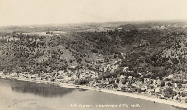 Caption reads: "Air View — Fountain City, Wis." Aerial view of town and surrounding landscape that includes trees, rolling hills, and a river.