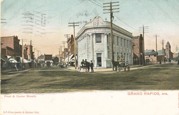 Colorized view of Front and Center Streets busy with people and a horse-drawn carriage, with a storefront's facade lining both streets. Caption reads: "Front & Center Streets. Grand Rapids, Wis."