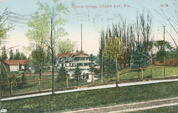 View from road toward Mineral Springs. There is a board sidewalk in the foreground. Caption reads: "Mineral Sprints, Green Bay, Wis."