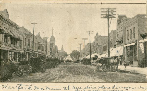 View of unpaved Main Street, with horse-drawn vehicles along the curbs.