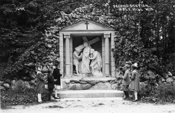 A group of children are praying with their hands clasped in front of them, at the second station of the cross on Holy Hill, near Hartford, Wisconsin. Caption reads: "Second Station, Holy Hill Wis."