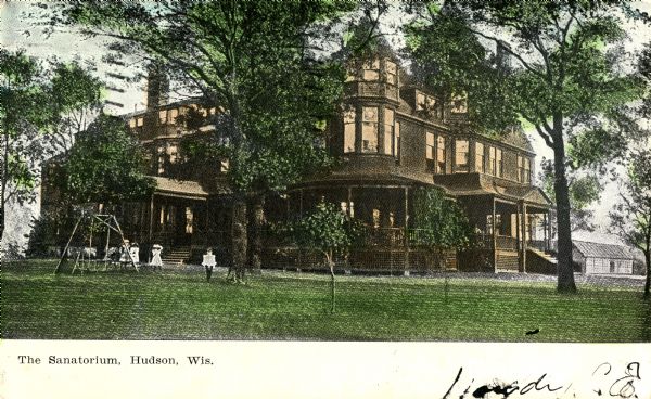 View across lawn towards the sanatorium. People are around a swing in the yard. Caption reads: "The Sanatorium, Hudson, Wis."