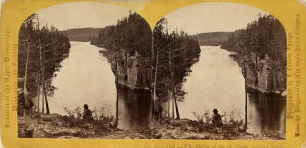 Stereograph of the Dalles rock formation with a two men in the foreground looking down at the Saint Croix River. On the left, one man stands leaning against a rock, and another man in the center sits at the edge of the cliff.