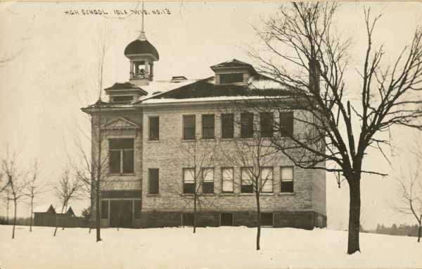 Exterior of high school building. There is a bell tower on the roof, and snow is on the ground. Caption reads: "High School, Iola Wis."