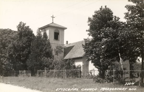 The Episcopal Church with surrounding wire fence and trees.