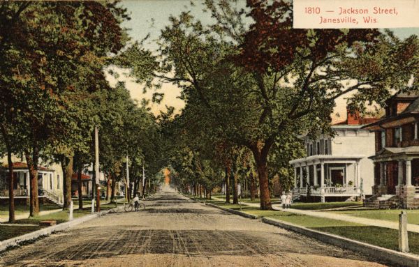 Residential view of Jackson Street. A person is standing in the street with a bicycle, and two people are walking along the sidewalk on the right. Caption reads: "Jackson Street, Janesville, Wis."
