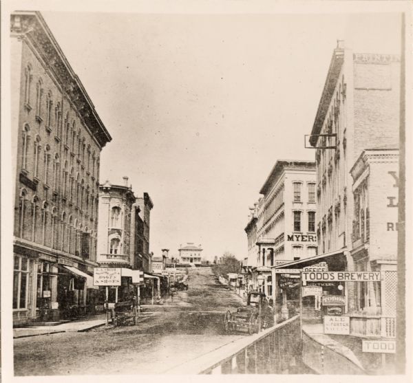 View from along right side of bridge of Milwaukee Street looking east in Janesville. The Myers House is located at the top of the hill. There is a sign for "Todds Brewery" on the right.