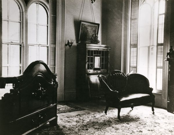 View of the Lincoln Bedroom. There is a bed on the left, and in the corner of the room is a desk and a chair. The tall windows are arched.
