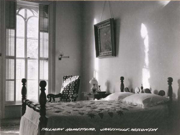 Interior view of a bedroom, with a tall, arched window on the far wall, and a painting hanging near the bed. Caption reads: "Tallman Homestead, Janesville, Wisconsin."