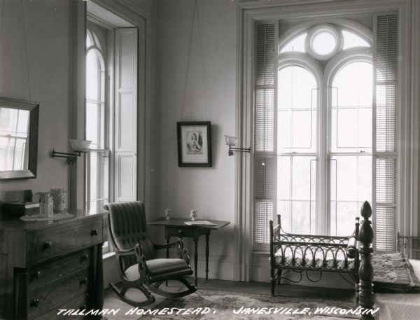 View of bedroom, with a baby crib in front of the window on the right, and a rocking chair in front of the window on the left. Caption reads: "Tallman Homestead, Janesville, Wisconsin".