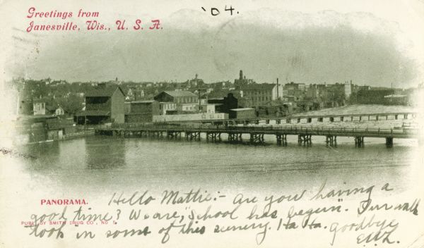 View across river and bridges towards Janesville. Caption reads: "Greetings from Janesville, Wis., U. S. A." Text at bottom reads: "Panorama."