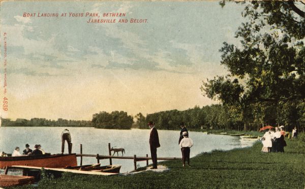 View towards people standing on the shoreline near a boat landing at Yosts Park. A man and a dog are standing on the pier, and a group of people are in a boat. Caption reads: "Boat Landing at Yosts Park, Between Janesville and Beloit."