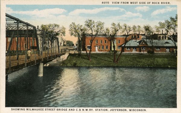 View with the Milwaukee Street Bridge on the left, and on the opposite shoreline is the Chicago & Northwestern Railway Station. Caption at top reads: "View from West Side of Rock River." Caption at bottom reads: "Showing Milwaukee Street Bridge and C & N. W. Ry. Station, Jefferson, Wisconsin."