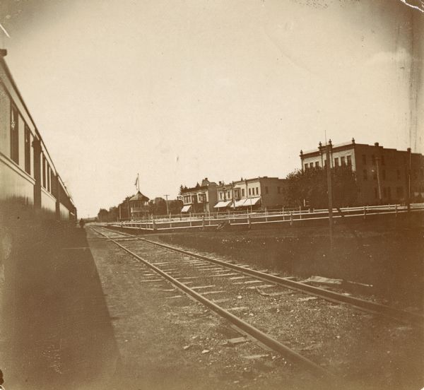 View from train platform looking back toward Johnson Creek businesses and houses. Railroad cars are on the left, and a set of railroad tracks are on the right.