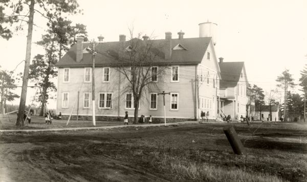 Indian boarding school at Lac du Flambeau Ojibwe Reservation. Children are in front of the building, and in the side yard.