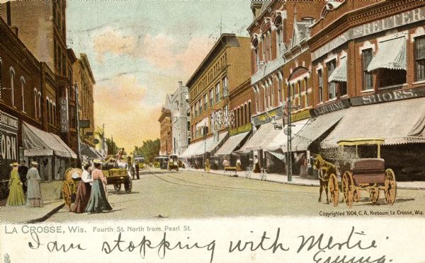 View down street. Horse-drawn vehicles and pedestrians are on the street and sidewalks. Streetcars are further down the street. Caption reads: "Fourth St. North from Pearl St., La Crosse, Wis."