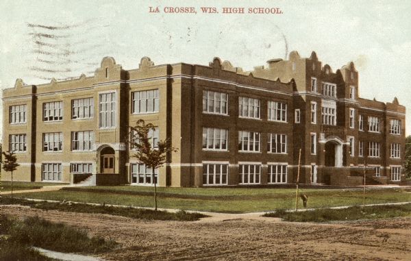 View across unpaved road toward the school on a corner. Caption reads: "La Crosse, Wis. High School."