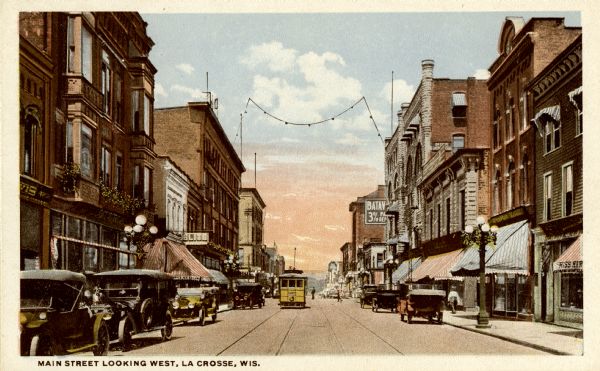 View down center of Main Street. Automobiles are parked at the curbs, and streetcar tracks are running up the street. Caption reads: "Main Street Looking West, La Crosse, Wis."
