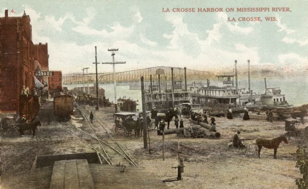 View from the top of a railroad car on railroad tracks along the Mississippi River shoreline. Ships are along the shoreline on the right, and railroad tracks and railroad cars are in the center along buildings on the left. A bridge over the river is in the background. Caption reads: "La Crosse Harbor on Mississippi River, La Crosse, Wis."