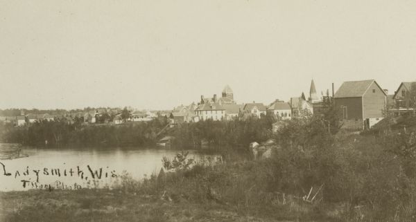 View towards Ladysmith. The river is on the left, and buildings are in the distance on the right. Caption reads: "Ladysmith, Wis."
