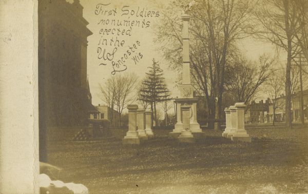 Caption reads: "First Soldier's Monuments Erected in the US — Lancaster Wis". There is a cannon and cannon balls on the lawn to the left of the monuments.