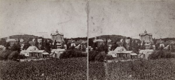 Stereograph of Lodi, Wisconsin. A field is in the foreground, and the town beyond and hills in the far background.