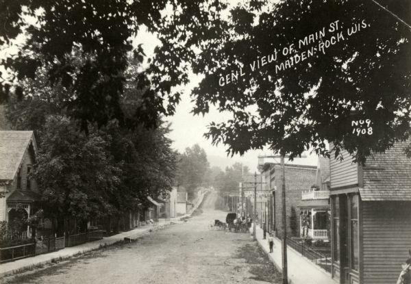 View down Main Street, with a horse-drawn vehicle further down on the right. Caption reads: "Genl View of Main St. Maiden Rock, Wis."