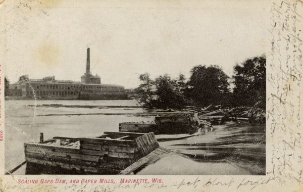 View of the Scaling Gaps dam in the foreground, and the paper mill in the background. Caption reads: "Scaling Gaps Dam and Paper Mills, Marinette, Wis."C