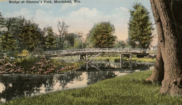 View from shoreline towards a bridge in Gleason's Park. Caption reads: "Bridge at Gleason's Park, Marshfield, Wis."