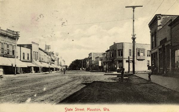 View down wide, unpaved street with businesses and storefronts on both sides. Caption reads: "State Street, Mauston, Wis."