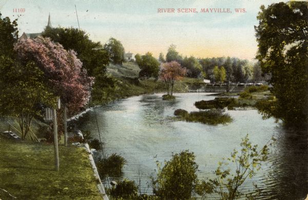 View from shoreline towards a river with a dam in the distance. Caption reads: "River Scene, Mayville, Wis."