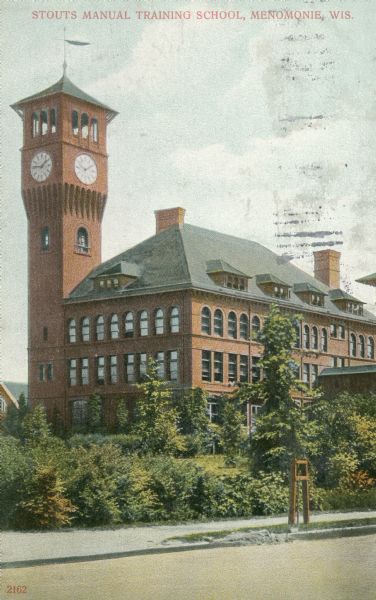 Stout State College Bowman Building with clock tower. It is attached to the central school building by a second-story bridge. Caption reads: "Stous Manual Training School, Menomonie, Wis."