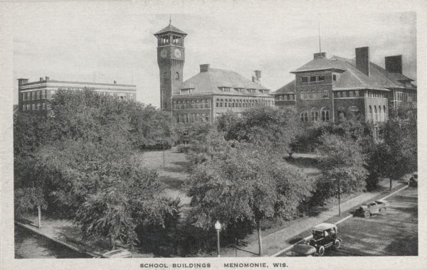 Elevated view of school buildings in Menomonie, later a part of the Stout State College. The building in the center has a clock tower. Caption reads: "School Buildings, Menomonie, Wis."