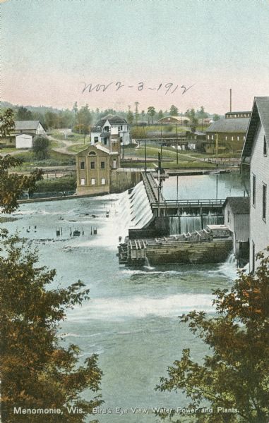 Elevated view of the dam and power plant on the Red Cedar River. Caption reads: "Menominie, Wis. Bird's Eye View, Water Power and Plants."